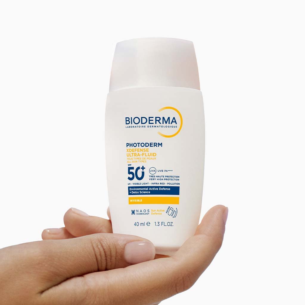 Bioderma sunscreen bottle held in a hand on a white background