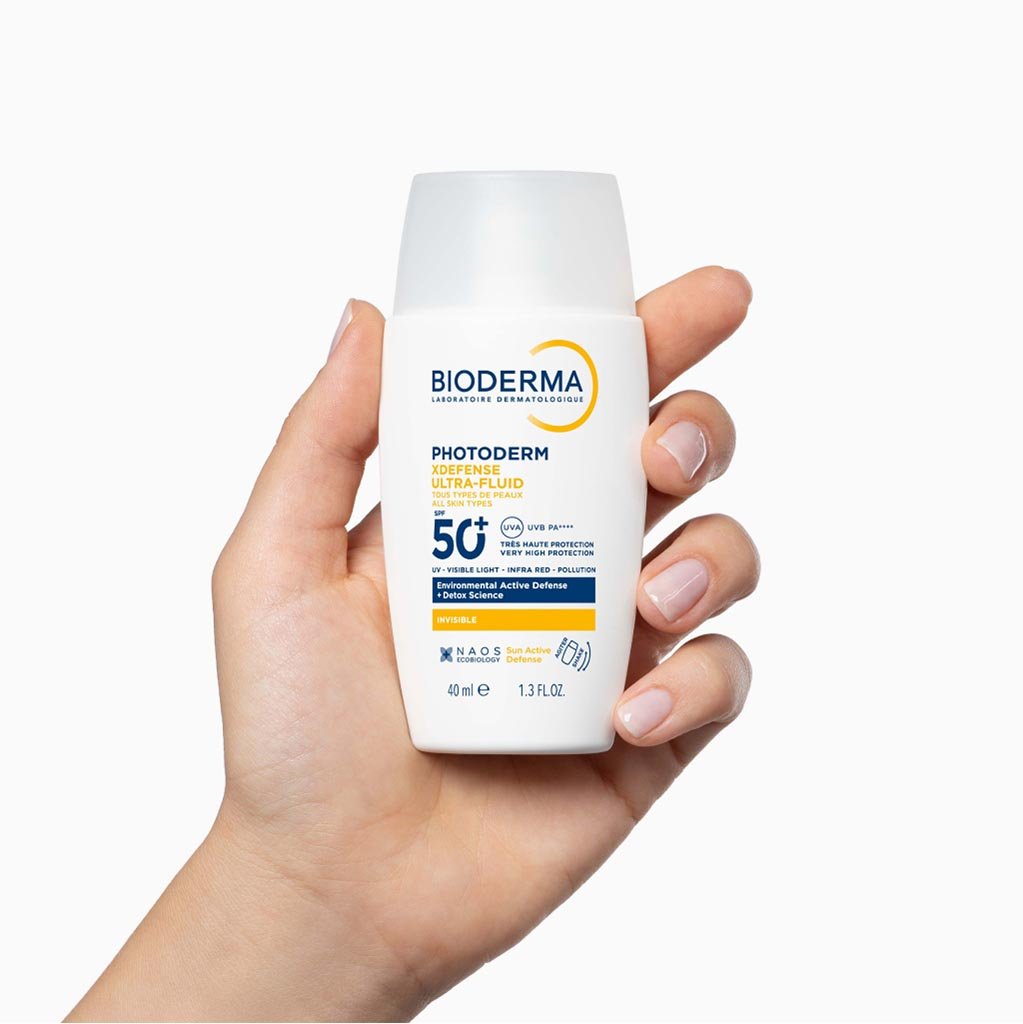 Hand holding a Bioderma sunscreen bottle on a white background